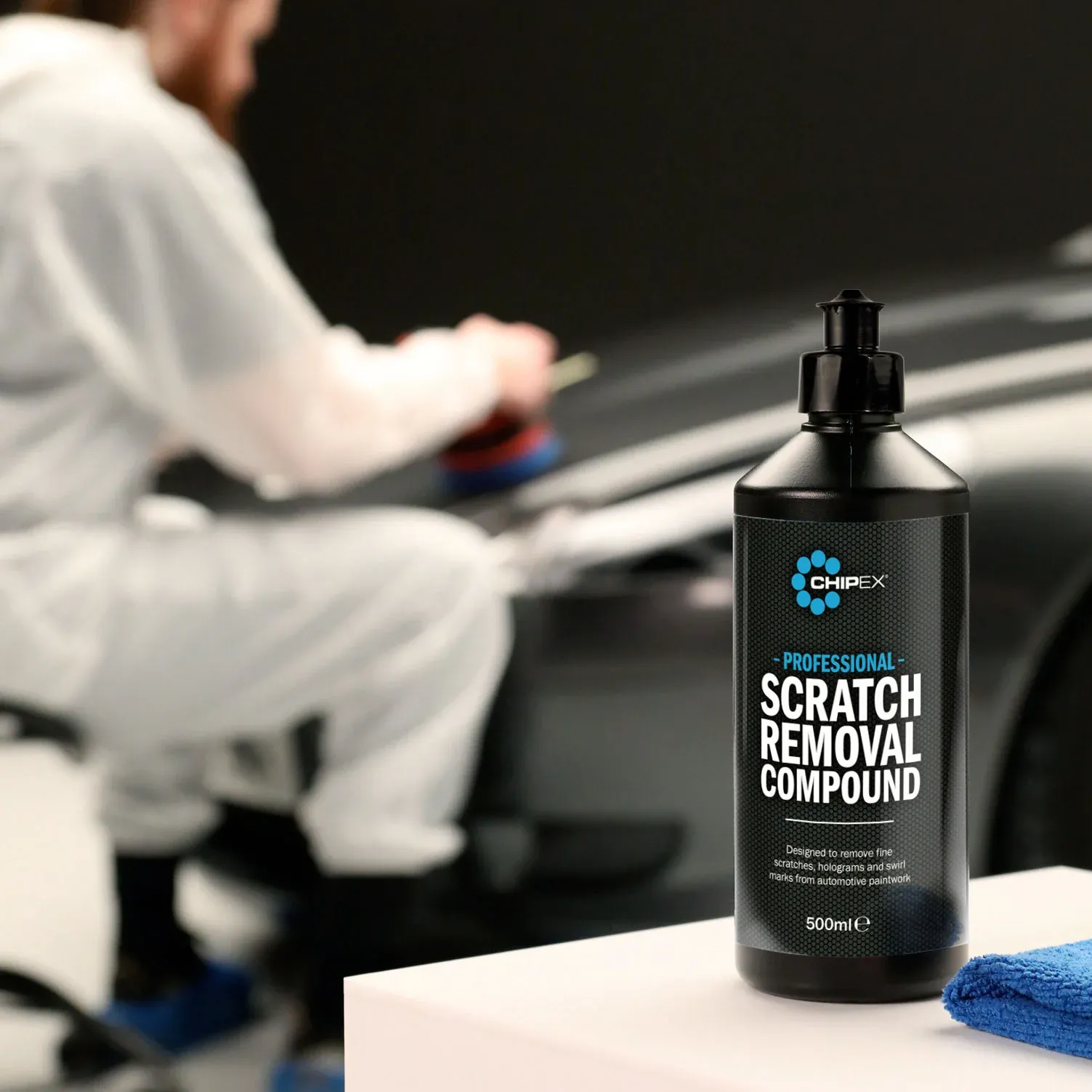 Foreground image of the Chipex Professional Scratch Removal Compound and person in the back in buffing out a car using the product
